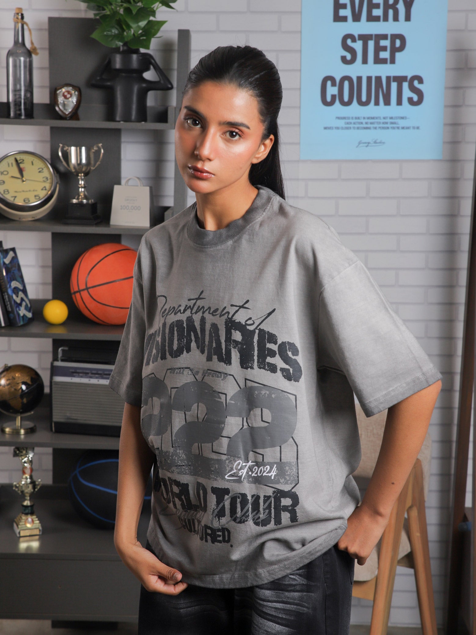 Close-up shot of female model wearing Cultured’s “222 World Tour” oversized t-shirt, styled in a lifestyle shoot with urban decor.