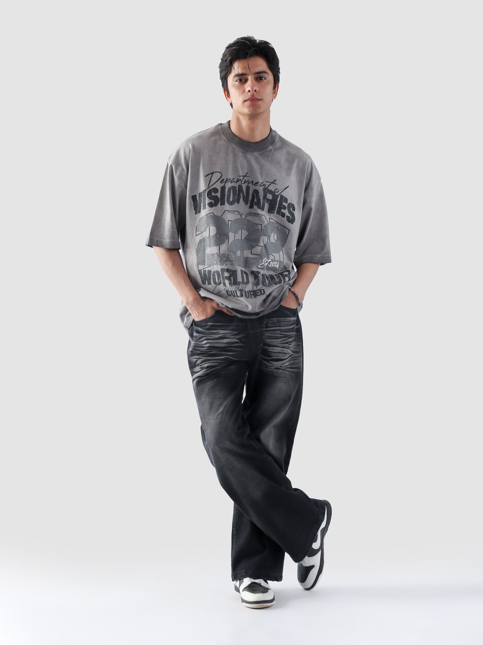 Male model crossing legs while wearing grey Cultured Visionaries oversized graphic tee with bold 222 print.