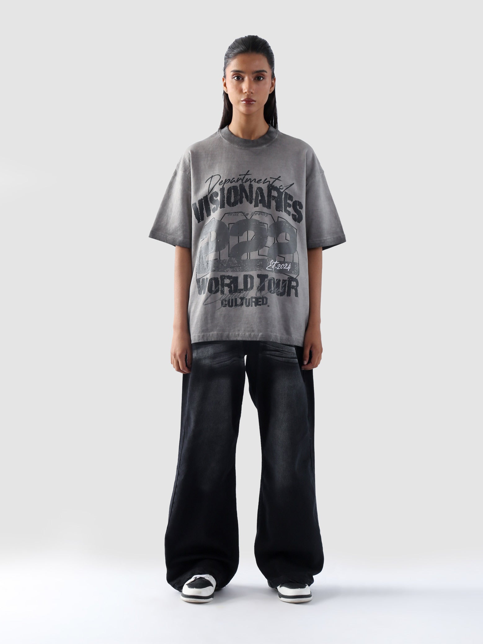Front-facing image of female model in Cultured’s grey “Dept. of Visionaries” oversized t-shirt and black wide-leg jeans.